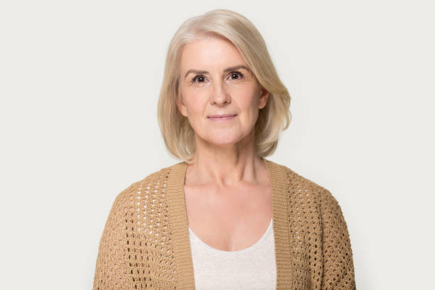 Head shot portrait attractive mature fifty year woman wearing brown knitted cardigan pose on grey studio background, healthy retired female natural beauty, health care, medical insurance concept image